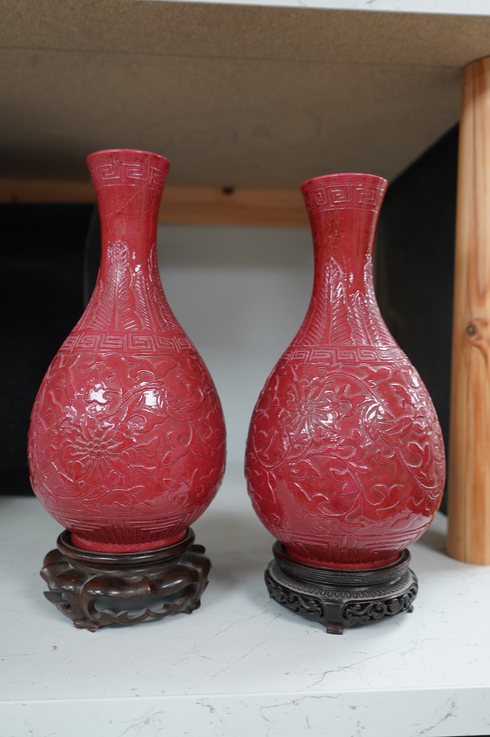 A pair of Chinese ruby ground ‘lotus’ bottle vases, late 19th century, each carved in relief with lotus flowers, scrolling tendrils and leaves, both with carved stands, 24cm high. Condition - one vase the neck broken bot